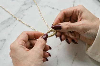 Femme aux ongles longs essayant de manipuler un fermoir mousqueton sur un collier en or, gros plan sur les mains